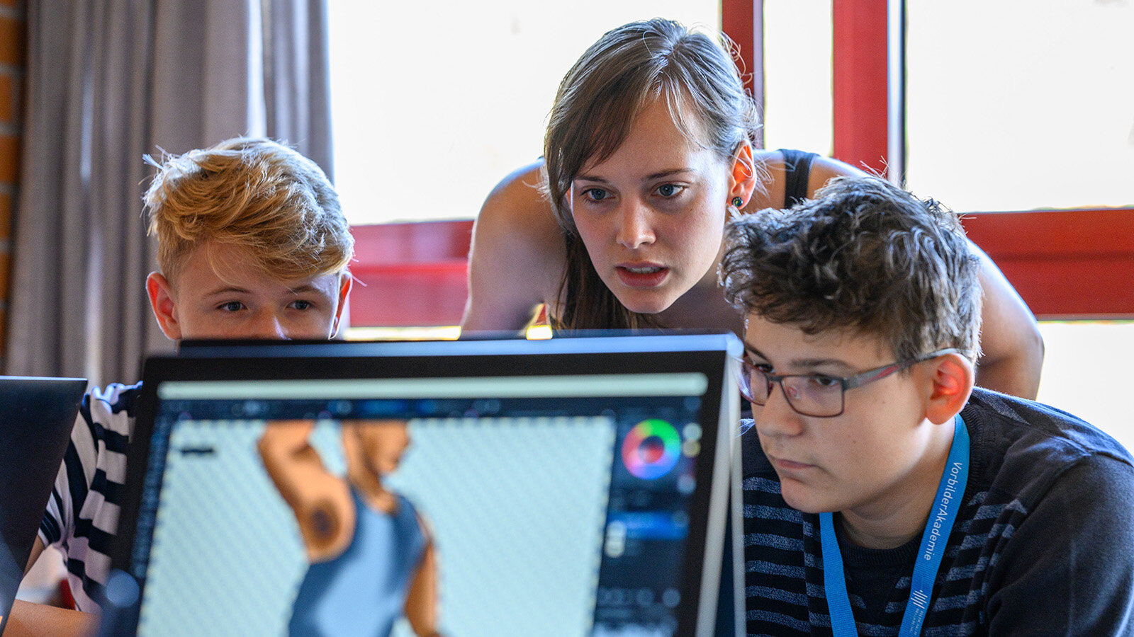 Eine junge Frau und zwei Jugendliche schauen konzentriert auf einen Computerbildschirm.